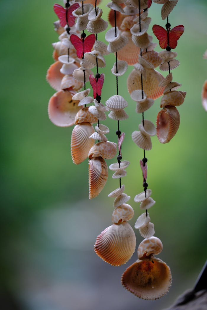 Artistic mobile featuring seashells and red butterflies against a blurred green backdrop.